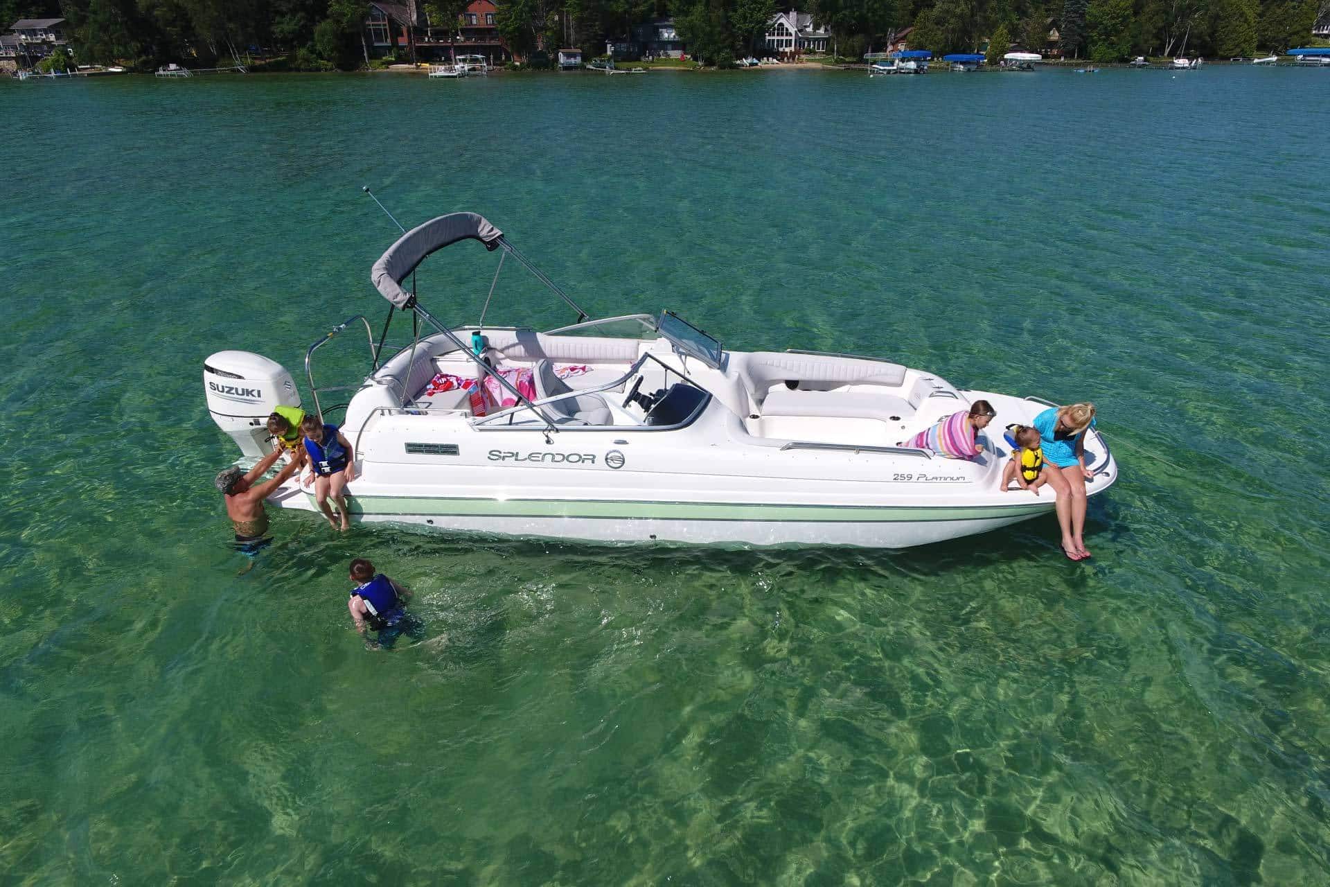 Family with young children swimming off the side of one of Splendor Boats' catamaran deck boats in shallow water.