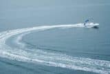 A catamaran deck boat speeding along a calm blue lake with a curved wake.