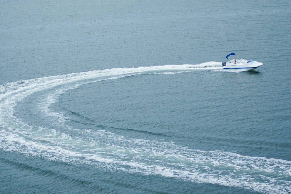 A catamaran deck boat speeding along a calm blue lake with a curved wake.